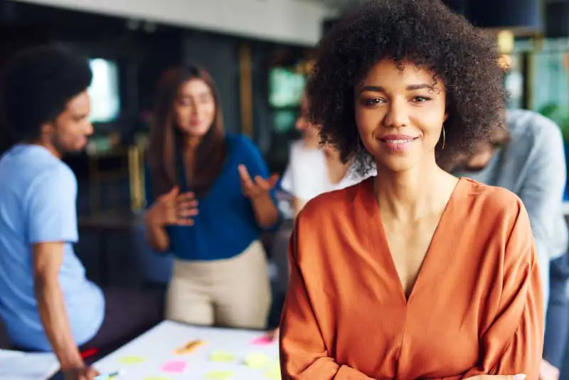 A woman looking straight at the camera smiling with people talking behind her.