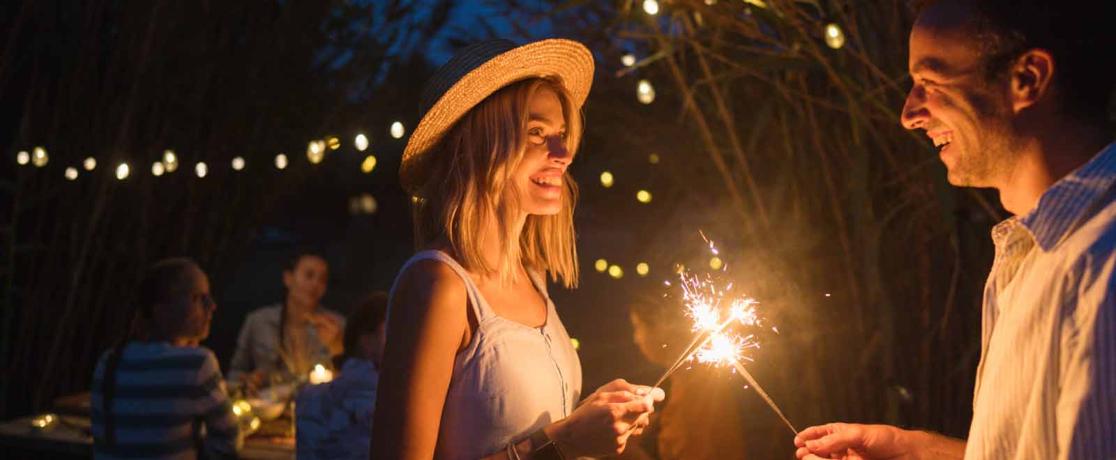 A couple enjoys a summer evening with sparklers, highlighting the joy and fun possible with smart summer savings.