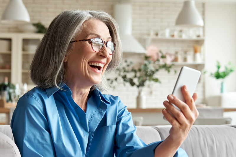 An older woman smiling holding a cell phone sitting on a couch