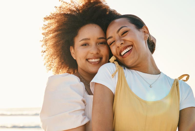 Two smiling women enjoying a sunny day at the beach, symbolizing the joy and freedom of saving money.