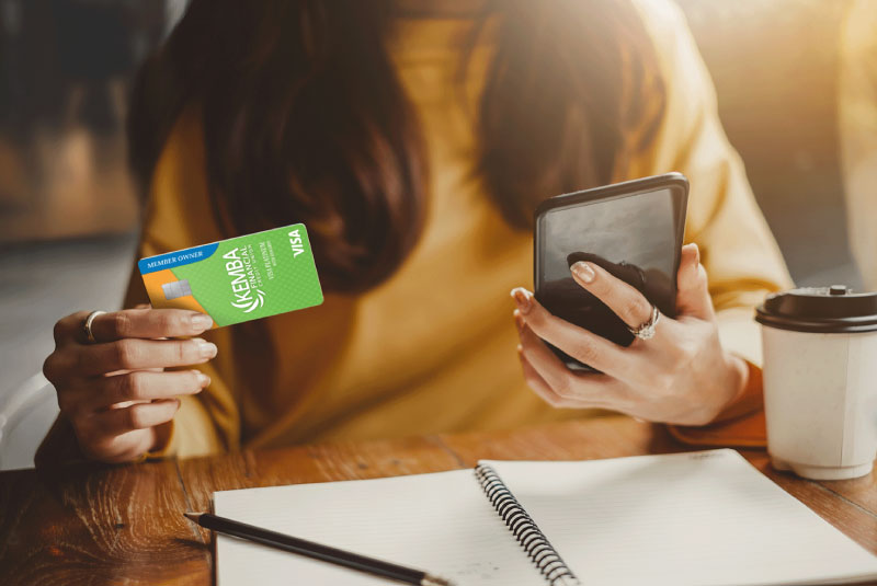 Person holding a KEMBA Visa Platinum Credit Card in one hand and a smartphone in the other
