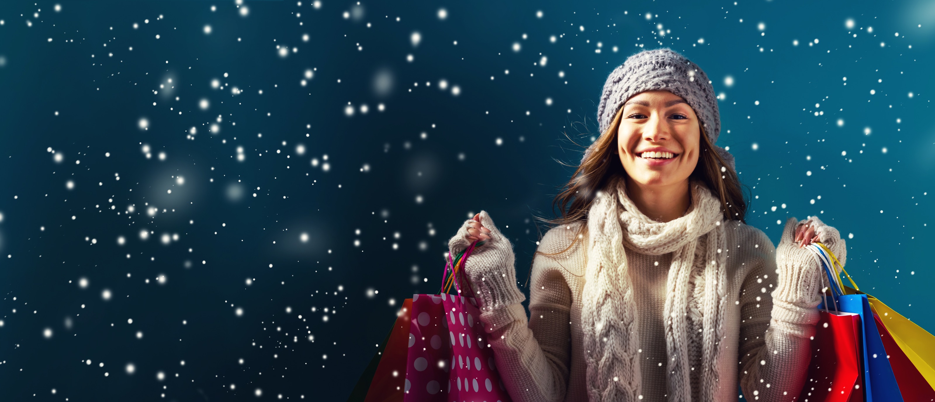 A woman walking in the snow and smiling with shopping bags in both of her hands.