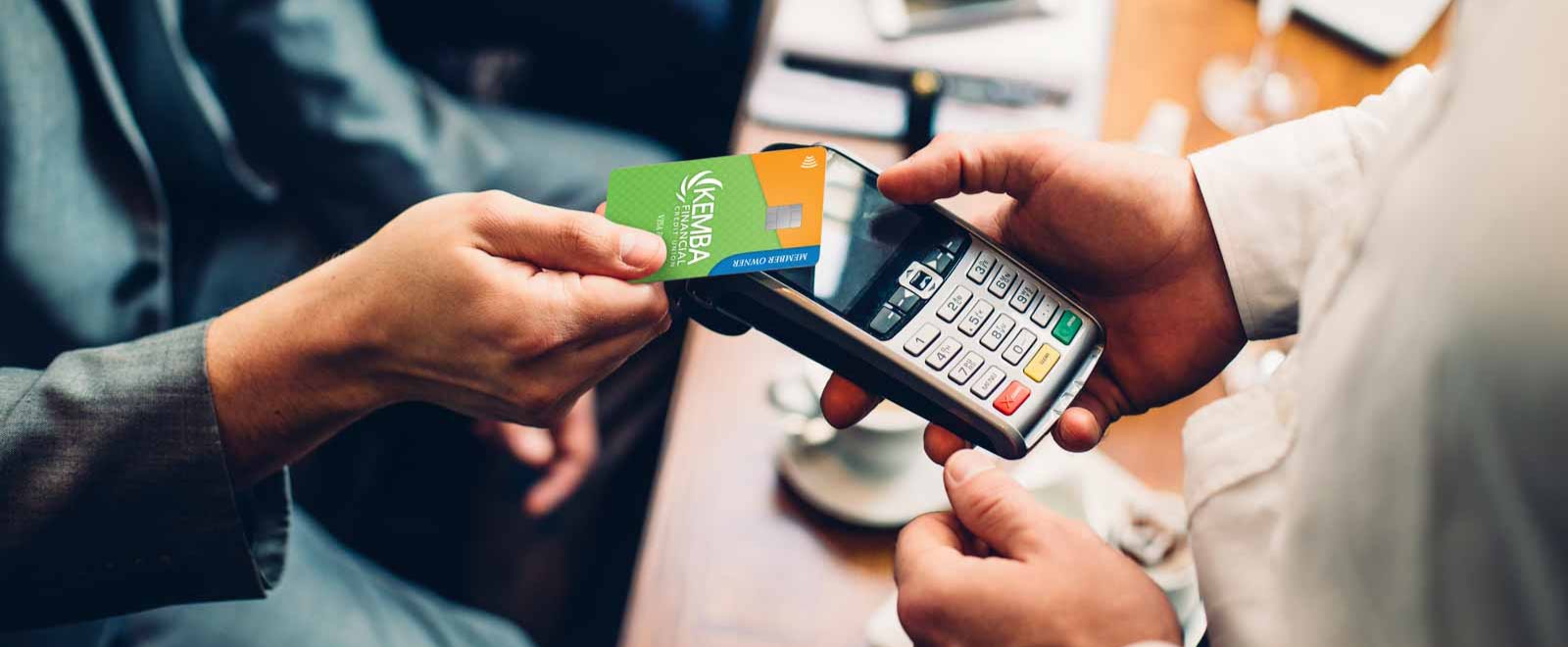Customer tapping KEMBA Financial Visa credit card for secure, contactless payment and earning cash back rewards.