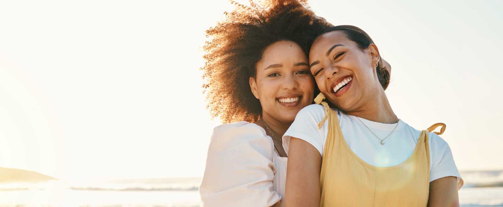 Two smiling women enjoying a sunny day at the beach, symbolizing the joy and freedom of saving money.