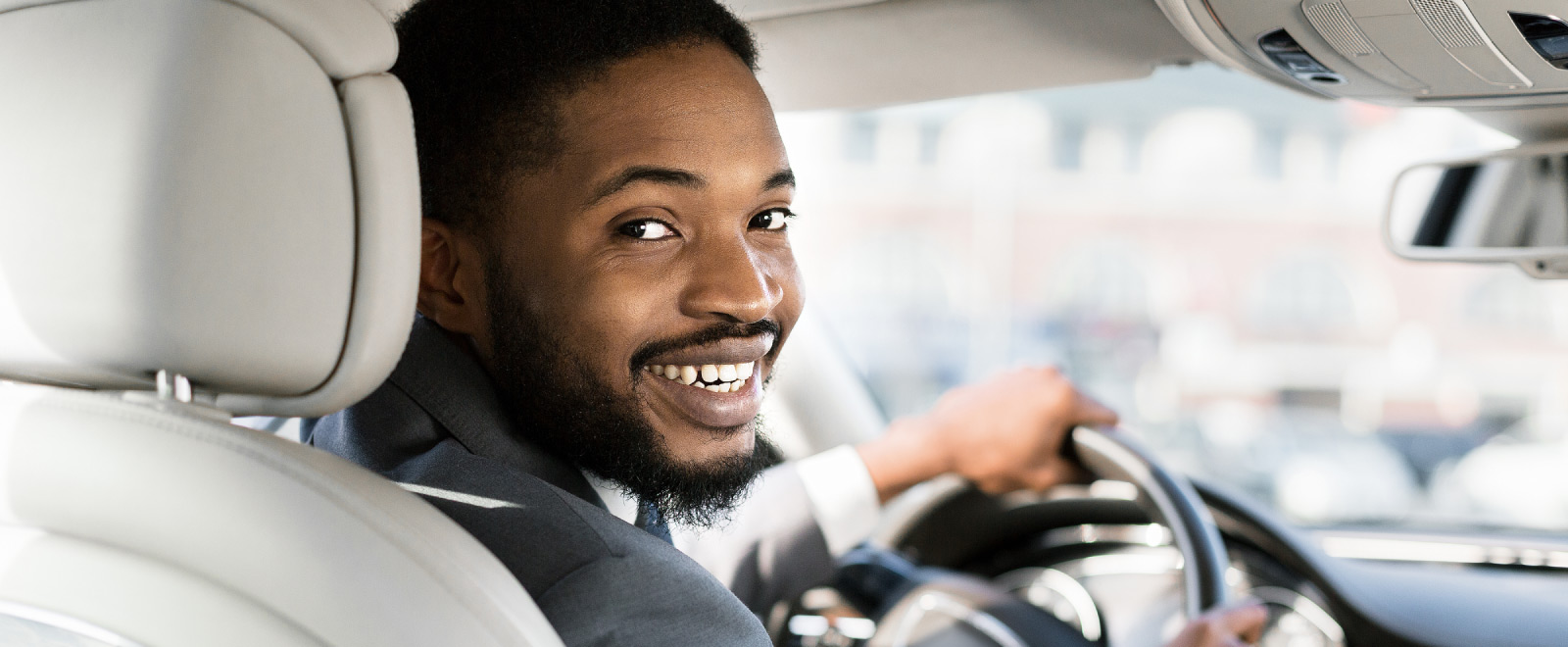 A man sitting in the drivers seat of a car, looking back and smiling. 