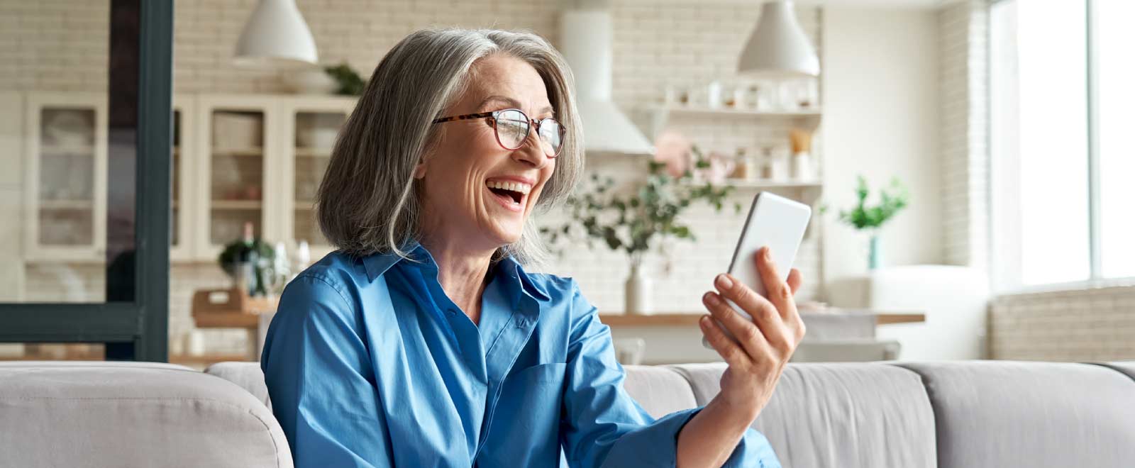 An older woman smiling holding a cell phone sitting on a couch