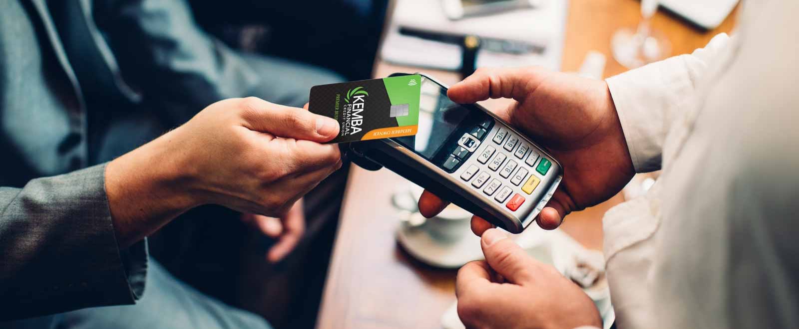 Customer tapping KEMBA Financial Visa Business credit card for secure, contactless payment and earning cash back rewards.